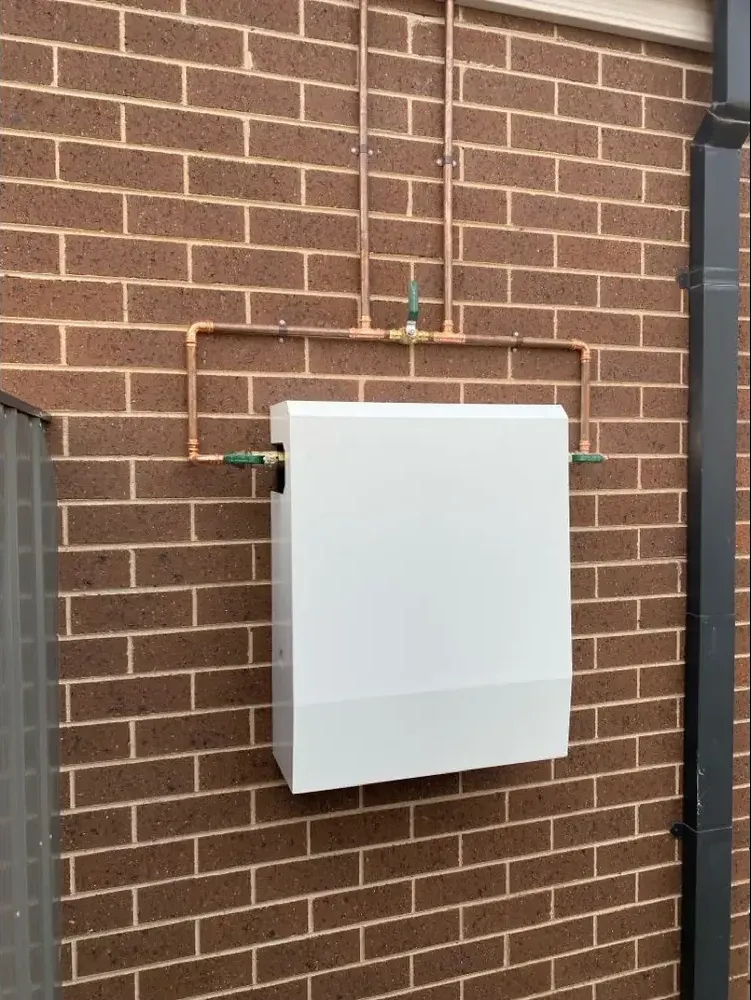 Whole-home water filtration system installed by NJZ Plumbing, plumber in the Macedon Ranges, with geometric copper pipework on a brick exterior wall