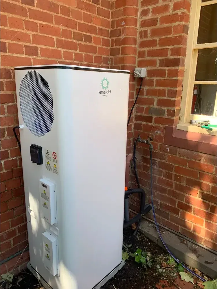 Heat pump hot water system installed against brick wall